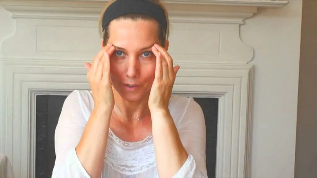 Woman demonstrating a facial massage technique by gently pressing her temples during an Anti-Aging Facial Oakton VA skincare treatment.